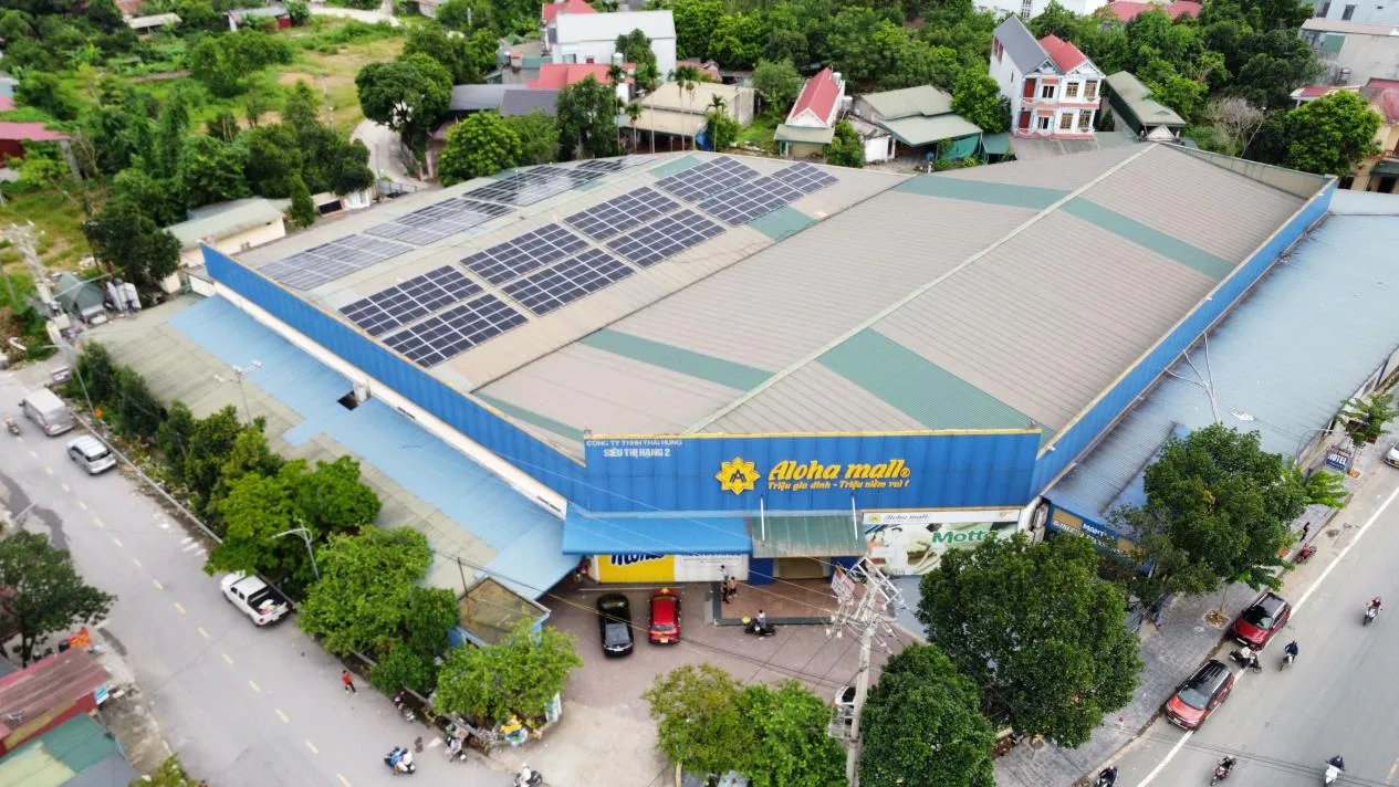 Aerial view of the Aloha Doan Hung commercial solar project in rural Vietnam, featuring a large warehouse building with rooftop solar panels and the "Aloha mall" storefront sign, supported by Hoymiles and BKE Vietnam.